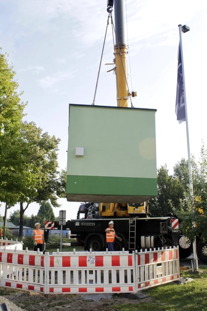 Arbeiter setzen mit einem Schwerlastkran einen DNS:NET Technikverteiler in Berlin-Altglienicke für den Glasfaser-Ausbau.