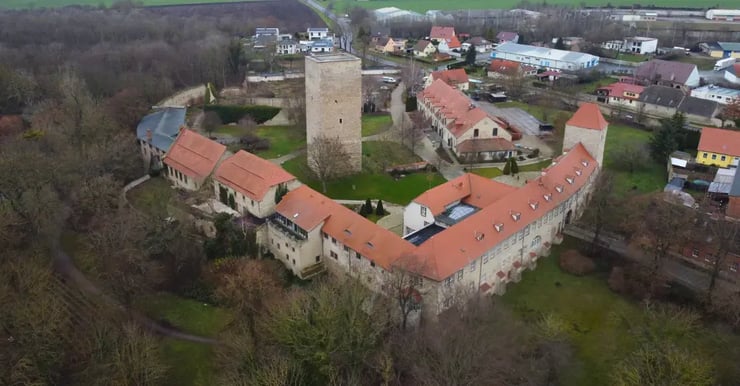 Luftaufnahme der Burg Wanzleben in Sachsen-Anhalt, umgeben von historischen Gebäuden mit roten Dächern und grünen Parkanlagen – Symbol für die Glasfaser-Versorgung der Börde-Region durch DNS:NET.