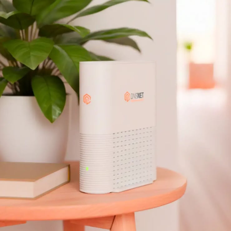 DNS:NET Premium-Repeater auf einem Tisch neben einer Pflanze für bessere WLAN-Reichweite zuhause.