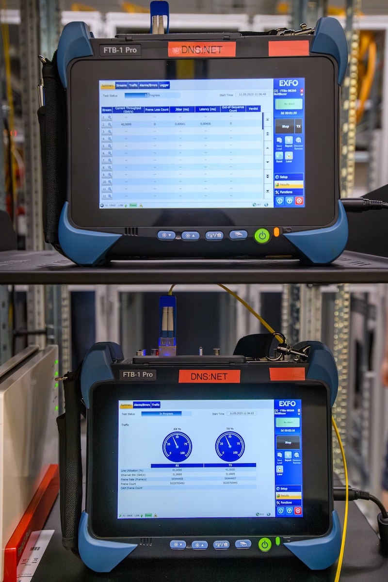 Zwei EXFO-Messgeräte vom Typ FTB-1 Pro mit DNS:NET-Label zeigen die Ergebnisse eines Glasfaser-Labortests. Auf den Displays sind Datenraten und Messwerte zu Latenz, Jitter und Durchsatz zu sehen – Teil der erfolgreichen 25 G-PON- und 50 G-PON-Tests von DNS:NET.
