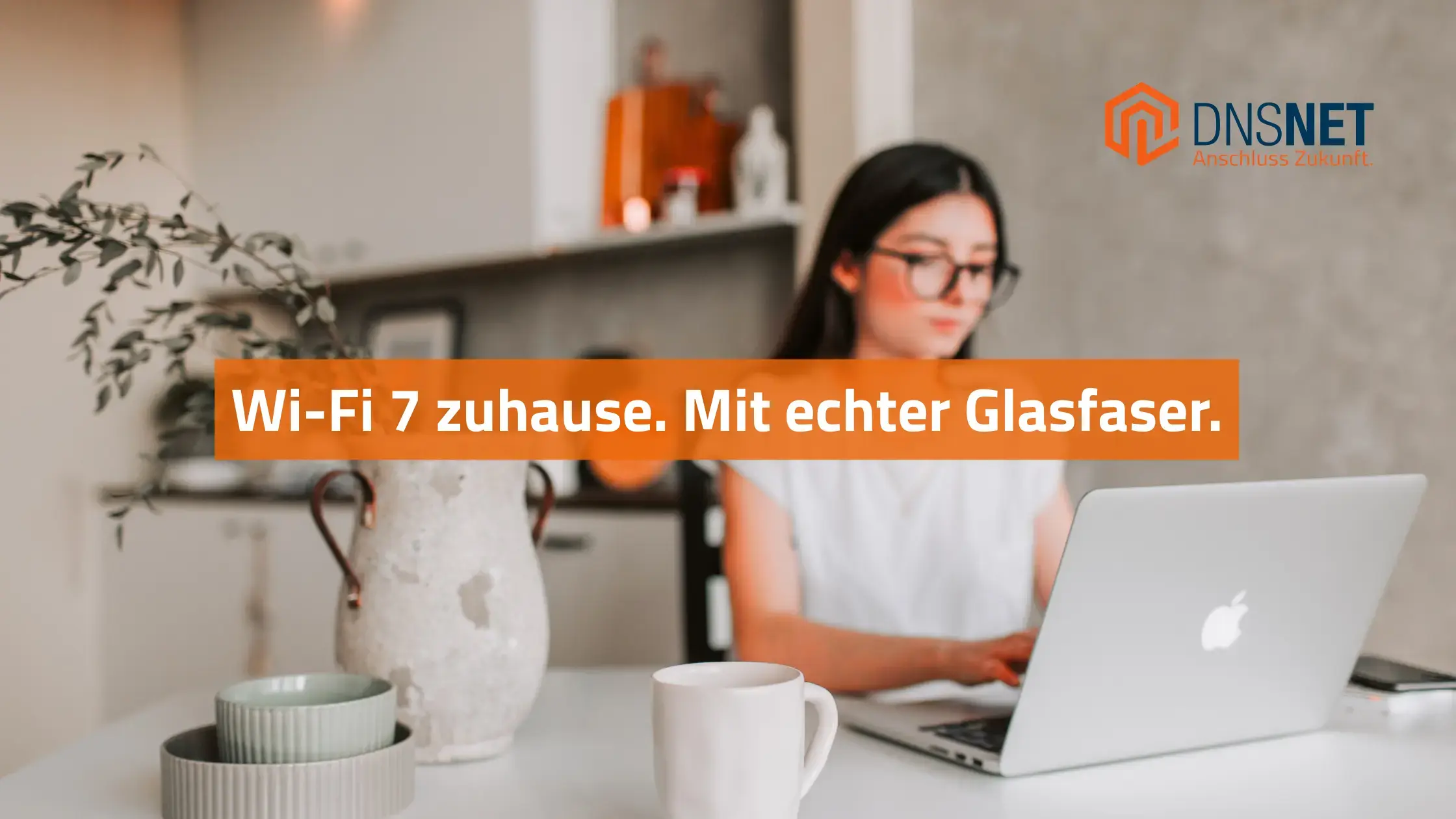 Frau arbeitet konzentriert im Homeoffice an einem Laptop in moderner Wohnung. Text im Banner: „Wi-Fi 7 zuhause. Mit echter Glasfaser.“ – DNS:NET Logo mit Claim „Anschluss Zukunft.“ sichtbar oben rechts.